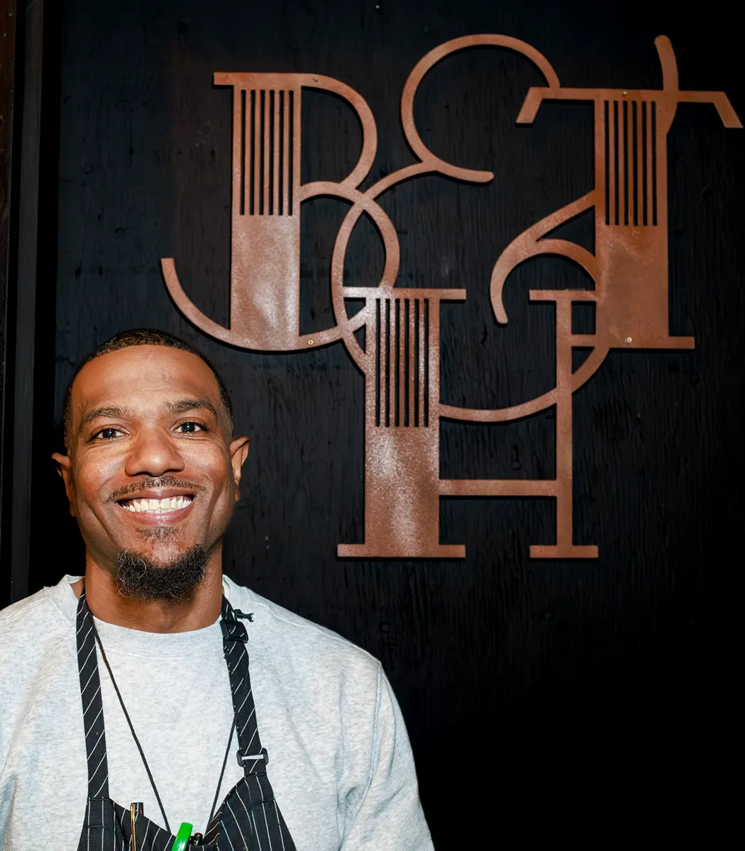 Chef Tay in a striped apron in front of the copper Black & Tan Hall monogram.