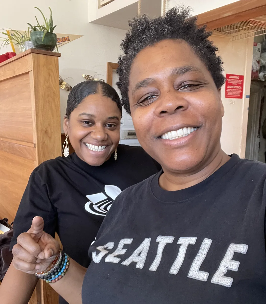 Erika White and Erika Kidd-White smiling together inside Fat&rsquo;s. One wears a Seattle T-shirt and points toward the camera.