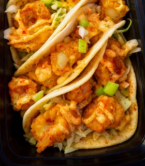 Crispy battered tacos in flour tortillas, topped with a creamy orange sauce, green onions and shredded cabbage, with a lime wedge.