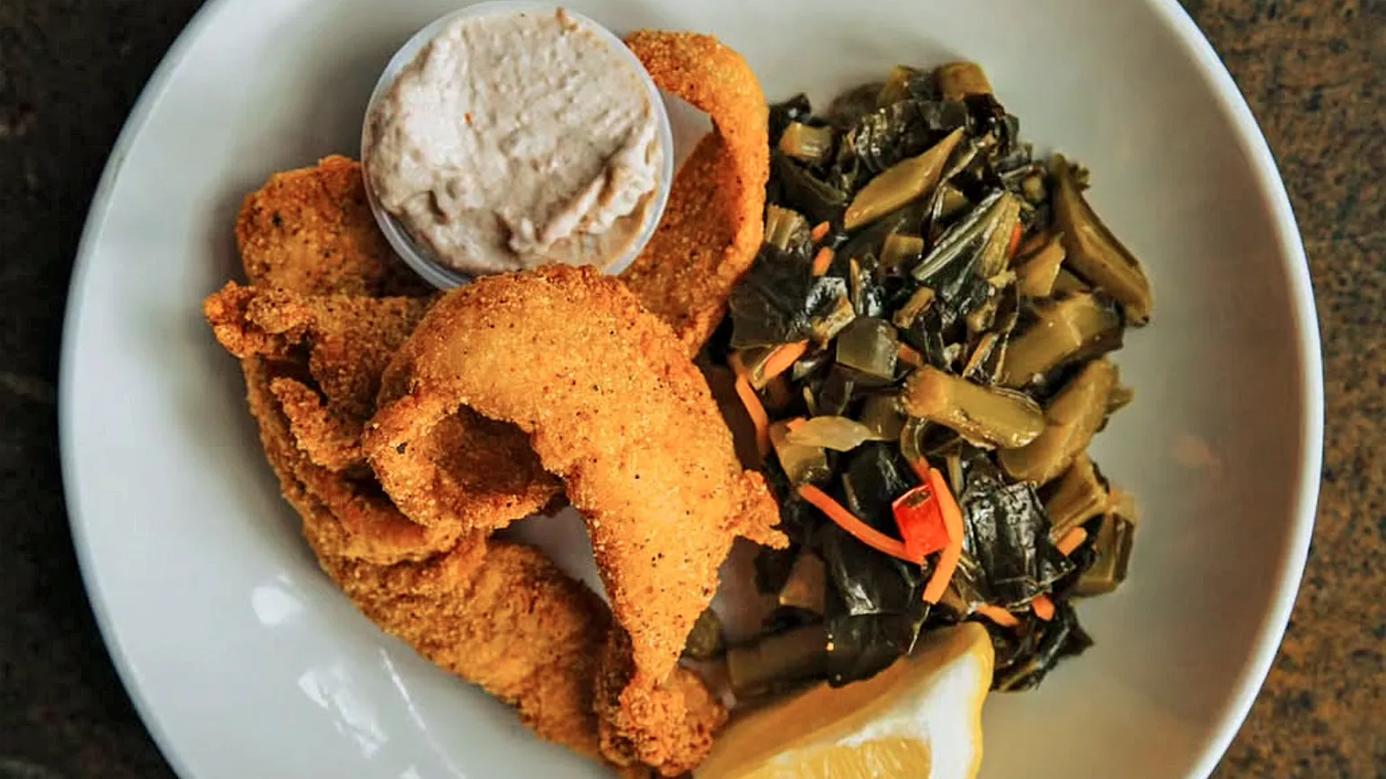 A plate of fried catfish with tartar sauce, collard greens and a lemon wedge from Island Soul.